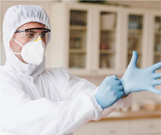Człowiek w kombinezonie ochronnym, zakładający rękawiczki w przygotowaniu do dezynfekcji