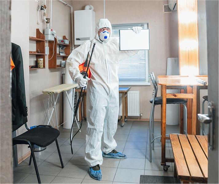 Człowiek w kombinezonie z odpowiednim sprzętem, przygotowujący się do oczyszczania pomieszczenia